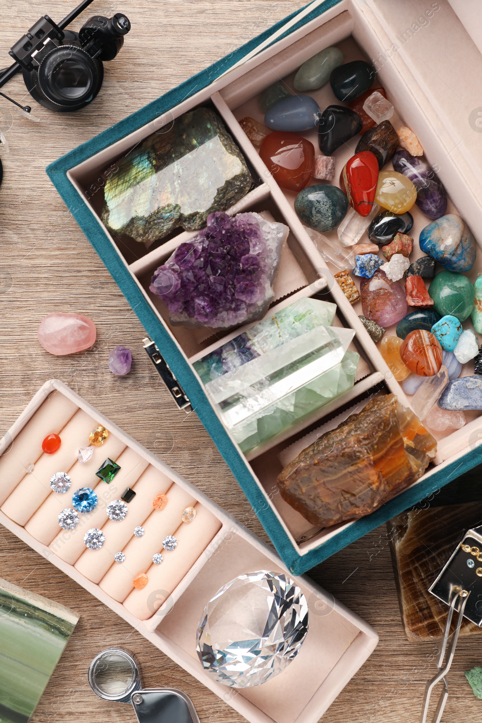 Photo of Box with beautiful gemstones and jeweler's tools on wooden table, flat lay