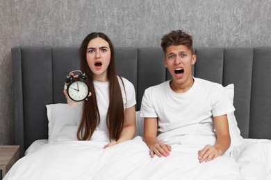 Photo of Shocked overslept couple with alarm clock in bed at home