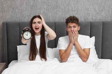 Photo of Shocked overslept couple with alarm clock in bed at home