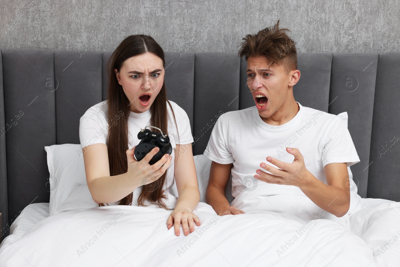 Photo of Shocked overslept couple looking at alarm clock in bed indoors