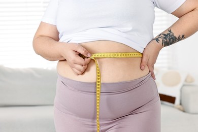 Photo of Weight loss. Plus size woman measuring waist with tape at home, closeup