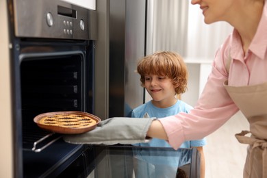 Photo of Mother and her son taking out pie from oven in kitchen, closeup