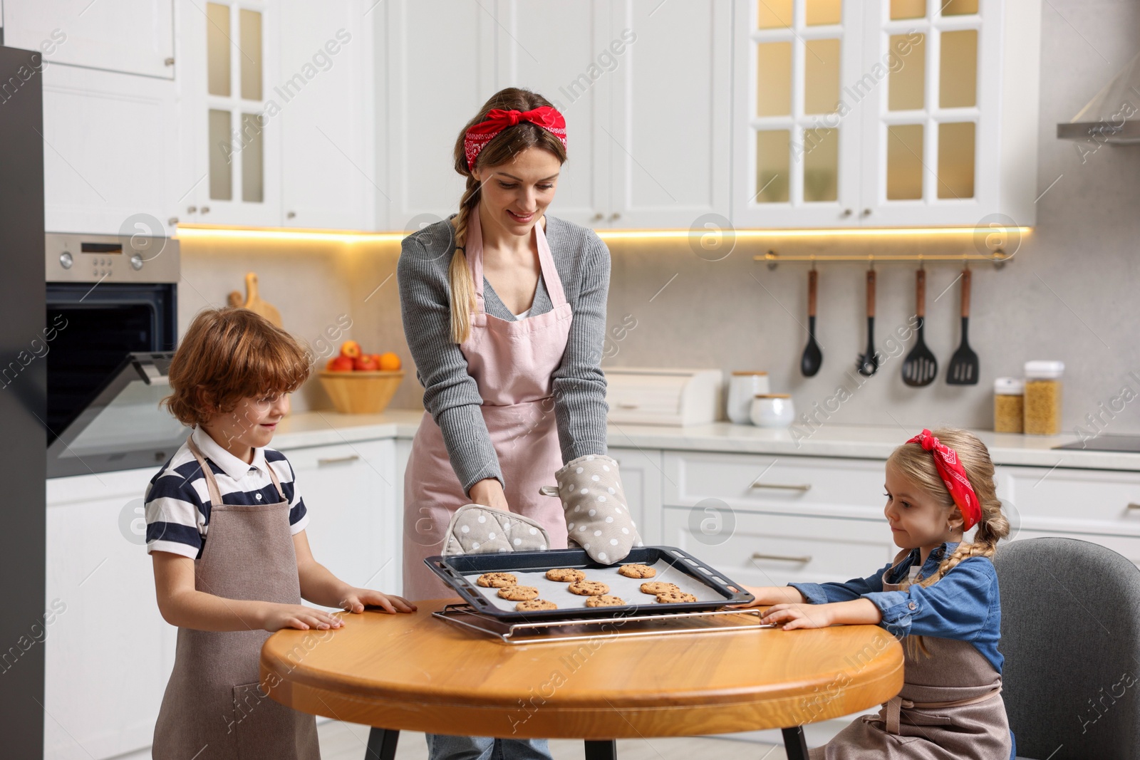 Photo of Mother and her kids with homemade cookies at wooden table in kitchen