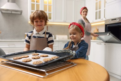 Photo of Cute kids with homemade cookies at wooden table in kitchen, selective focus. Woman baking indoors