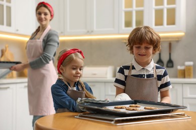 Photo of Cute kids with homemade cookies at wooden table in kitchen, selective focus. Woman baking indoors