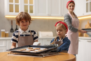 Photo of Cute kids with homemade cookies at wooden table in kitchen, selective focus. Woman baking indoors