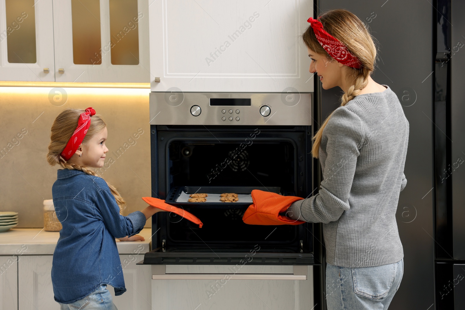 Photo of Mother and her daughter taking out buns from oven in kitchen