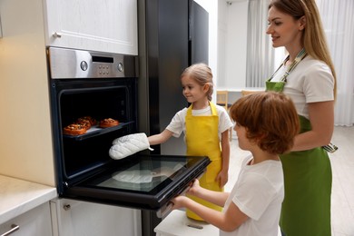 Photo of Mother and her kids taking out buns from oven in kitchen