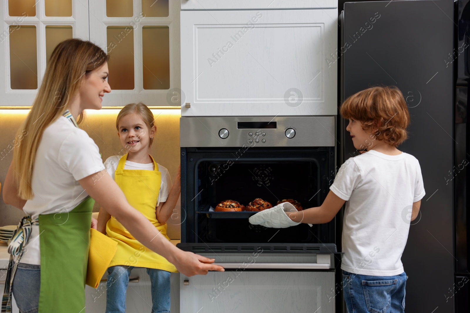 Photo of Mother and her kids taking out buns from oven in kitchen