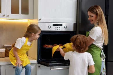 Photo of Mother and her kids taking out buns from oven in kitchen