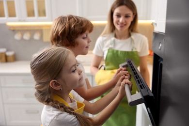 Photo of Mother and her kids baking food in oven indoors, selective focus