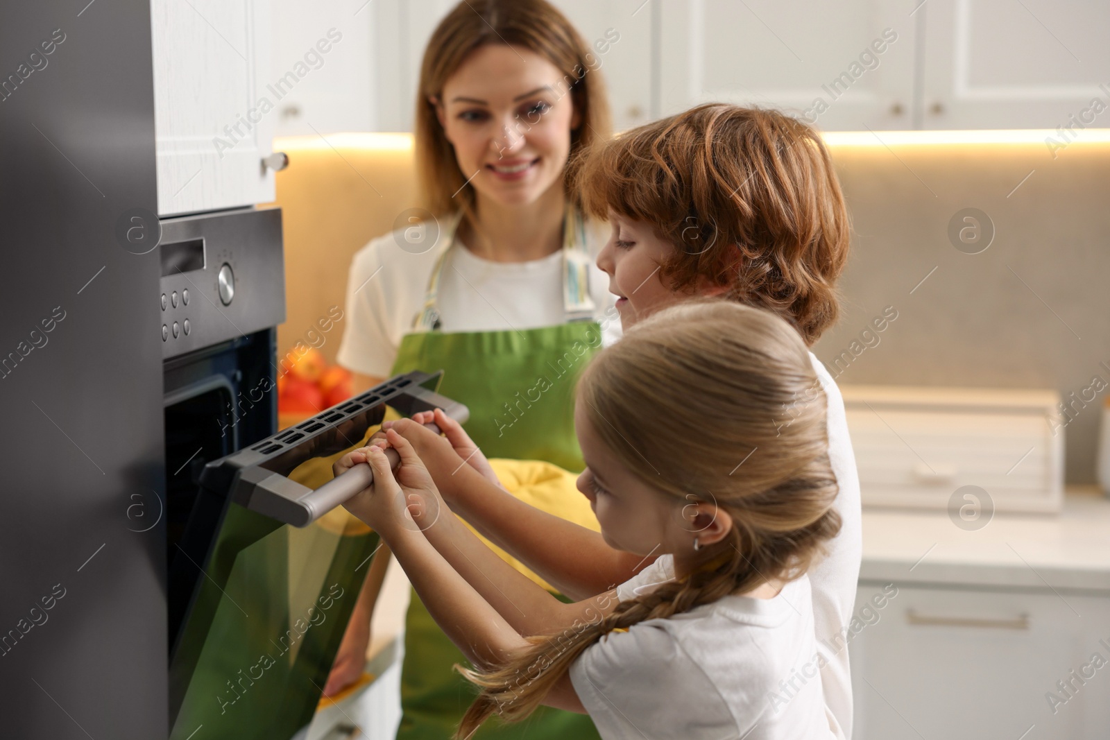 Photo of Mother and her kids baking food in oven indoors, selective focus