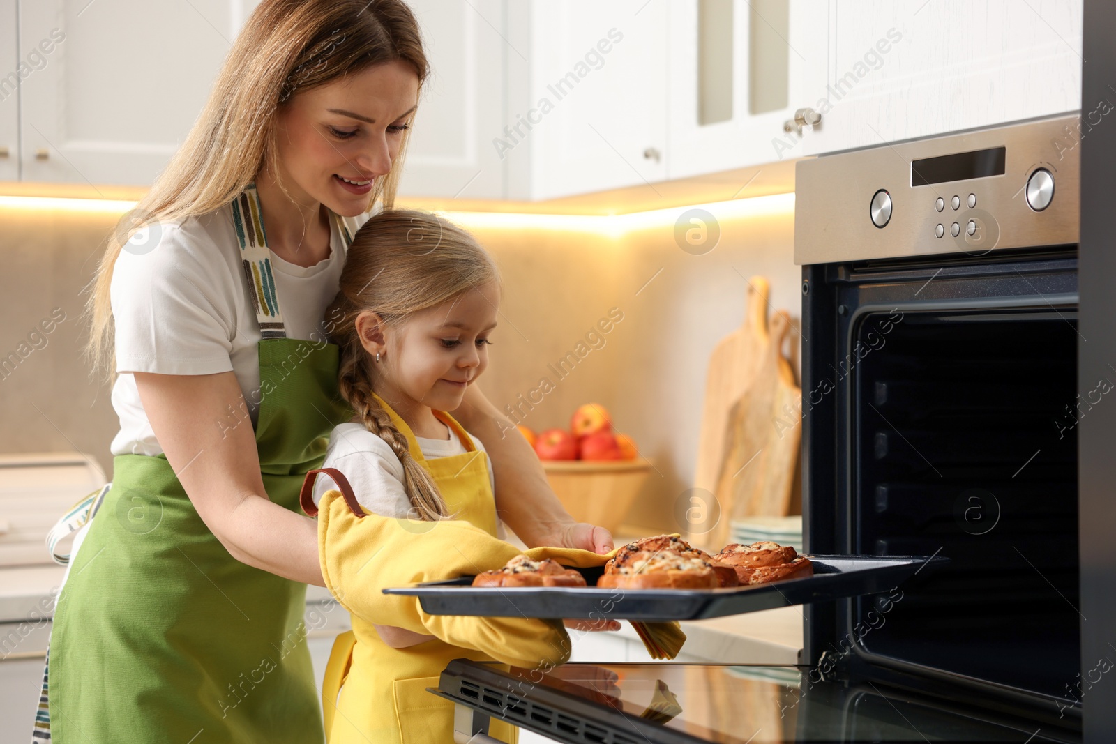 Photo of Mother and her daughter taking out buns from oven in kitchen