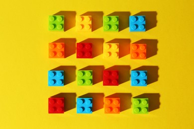 Photo of Construction toy. Colorful building bricks on yellow background, flat lay