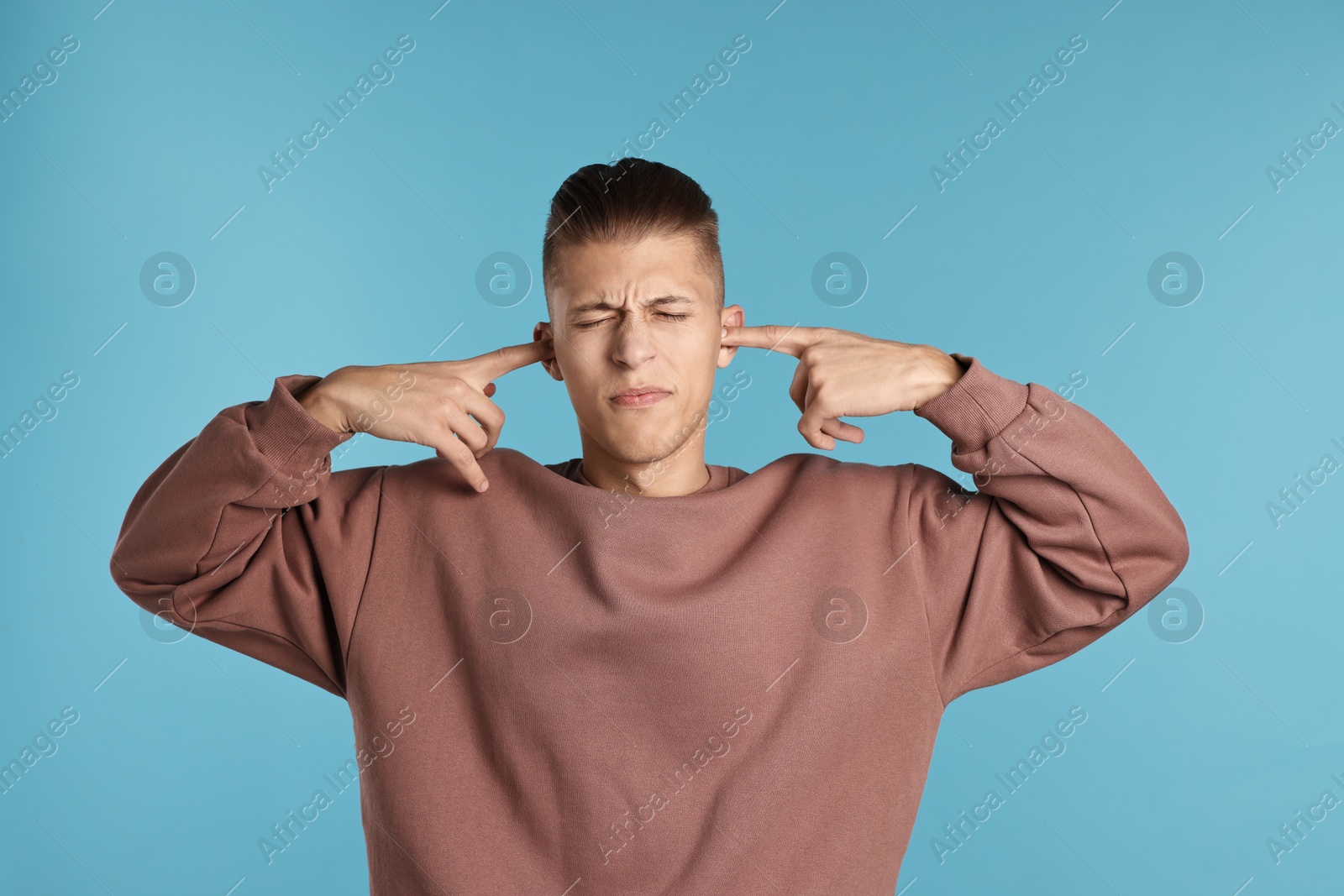 Photo of Annoyed young man covering his ears due to loud sound on light blue background