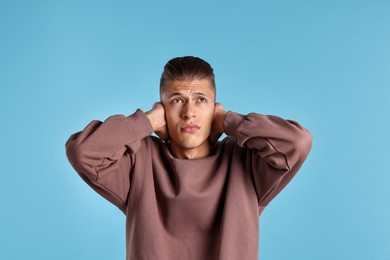 Photo of Annoyed young man covering his ears due to loud sound on light blue background