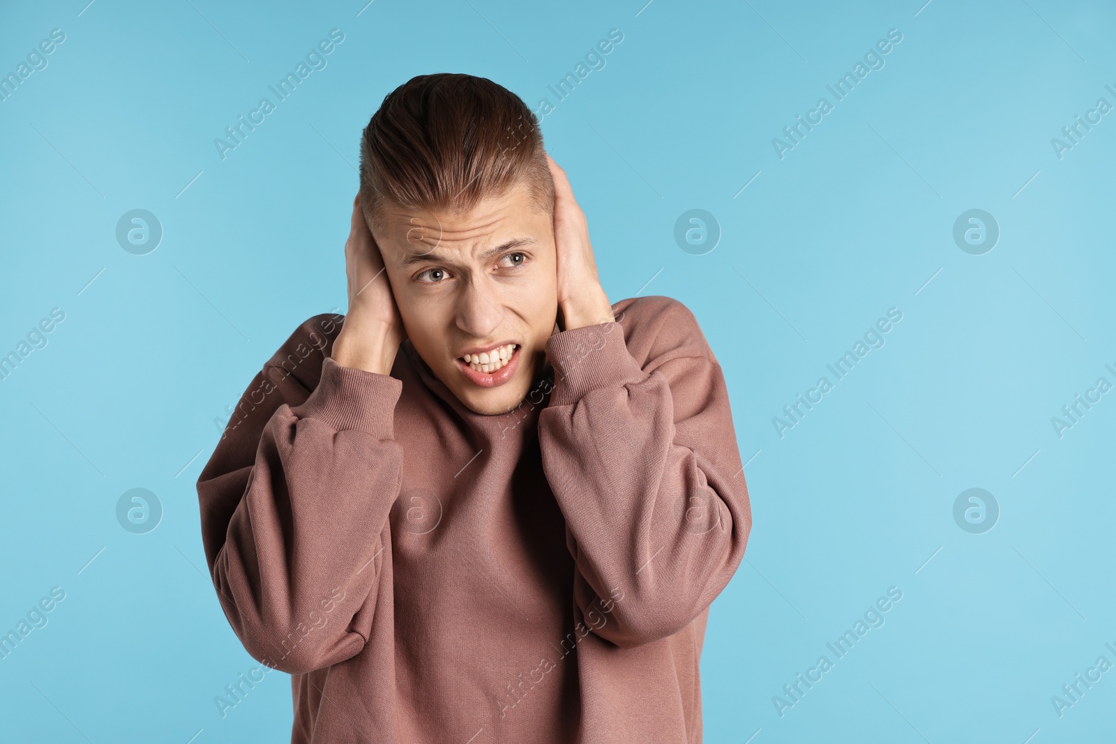 Photo of Annoyed young man covering his ears due to loud sound on light blue background