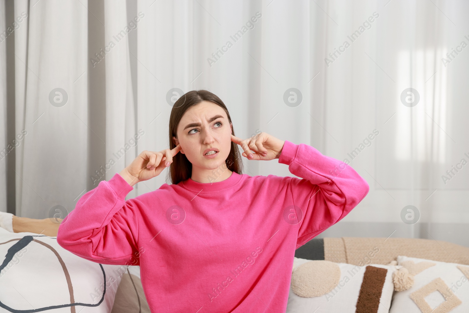 Photo of Annoyed woman covering her ears from loud noise at home