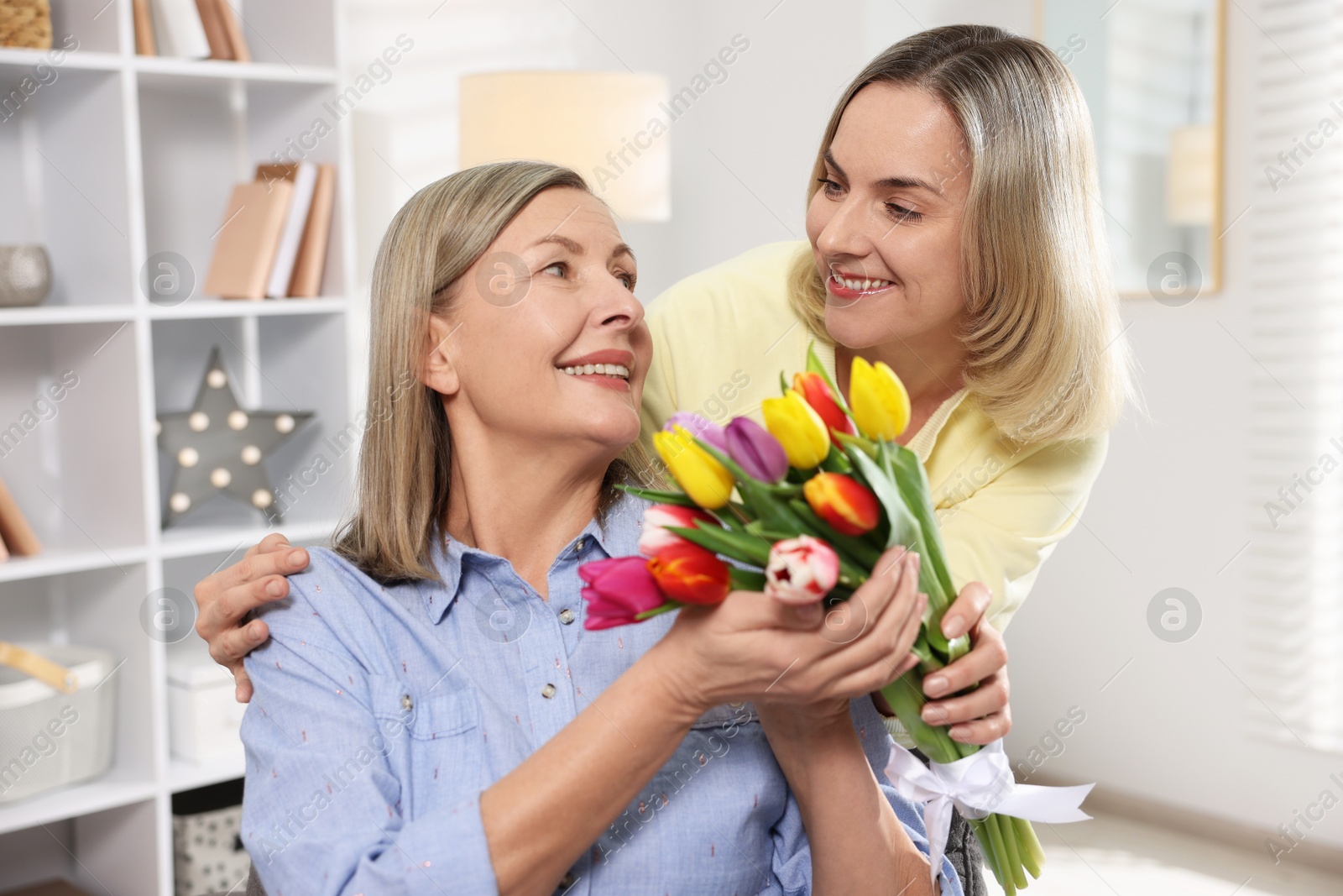 Photo of Smiling daughter congratulating her mom with bouquet of tulips at home. Happy Mother's Day