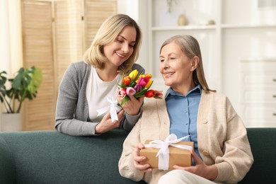 Photo of Smiling daughter congratulating her mom with bouquet of tulips and gift at home. Happy Mother's Day