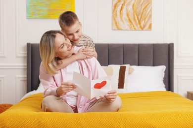 Photo of Happy Mother's Day. Son greeting his mom with card on bed indoors. Space for text