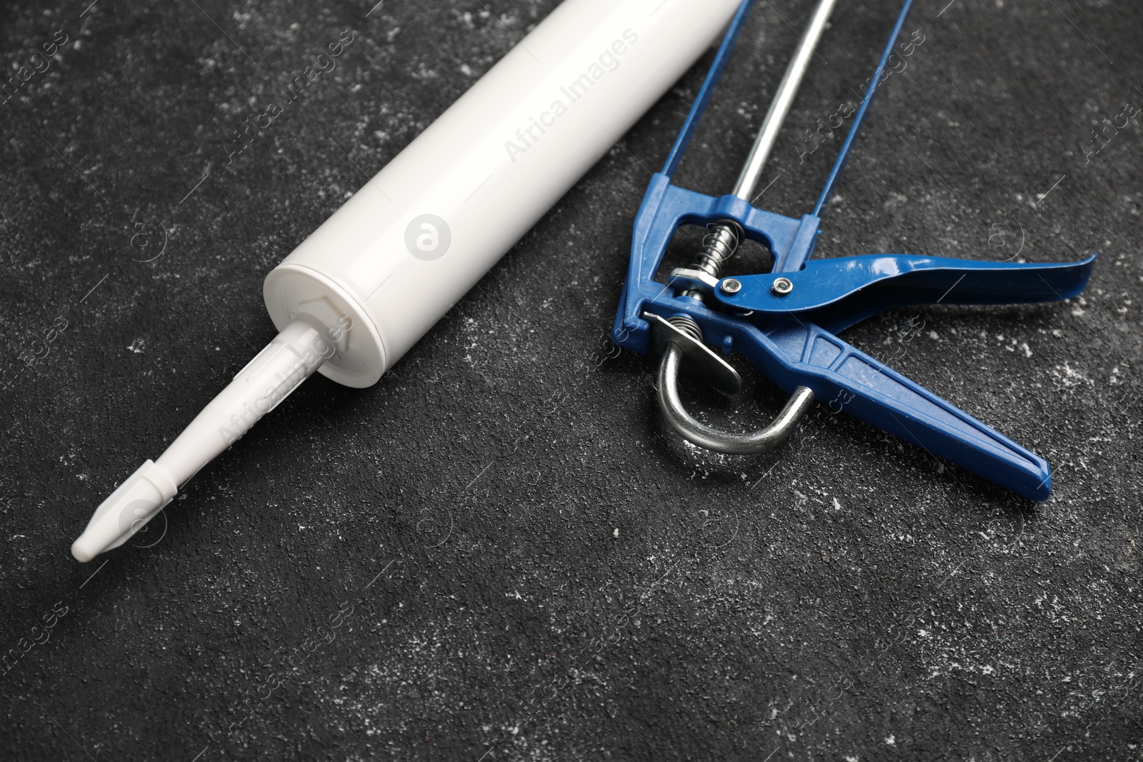 Photo of Glue gun and tube on black textured background, closeup