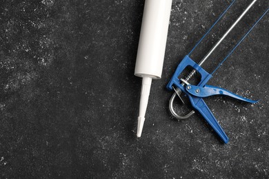 Glue gun and tube on black textured background, top view. Space for text