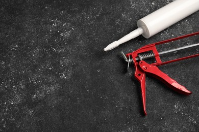 Glue gun and tube on black textured background. Space for text