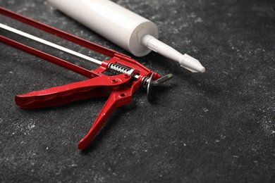 Glue gun and tube on black textured background, closeup