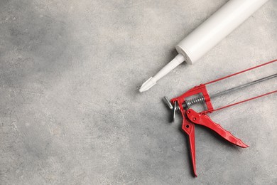 Photo of Glue gun and tube on grey background, top view. Space for text