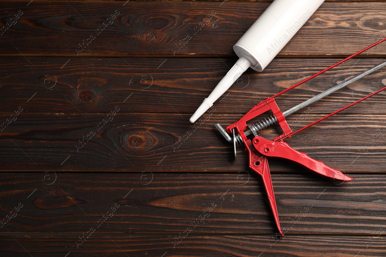 Photo of Glue gun and tube on wooden background, top view. Space for text