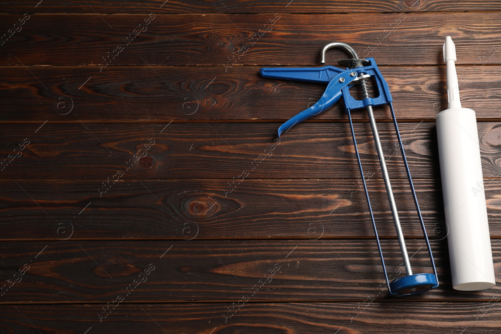 Photo of Glue gun and tube on wooden background, top view. Space for text