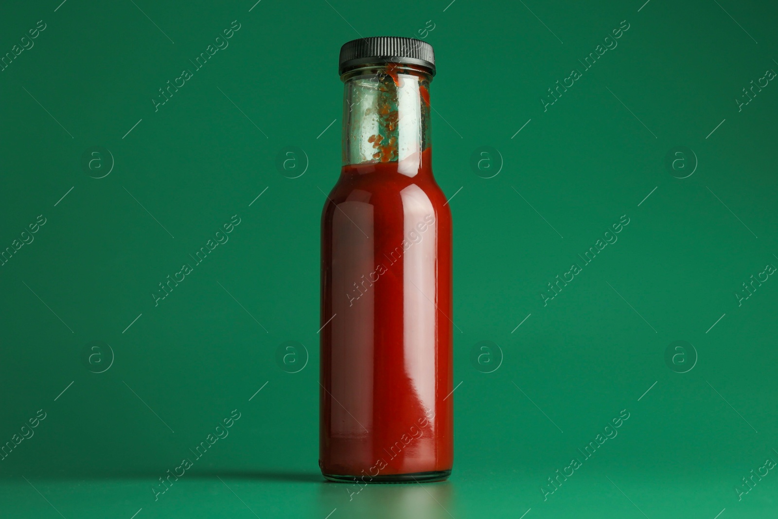 Photo of Tasty ketchup in bottle on green background