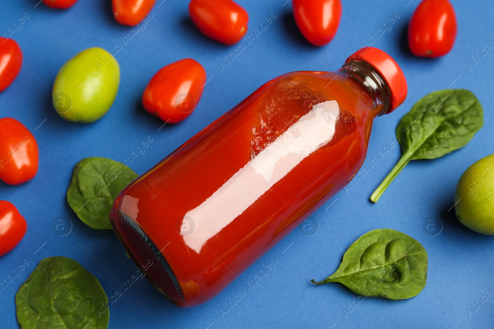 Photo of Tasty ketchup in bottle, tomatoes and basil on blue background, closeup