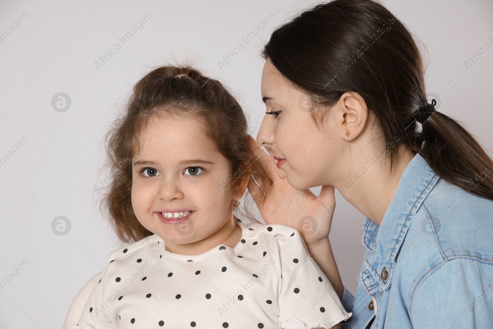 Photo of Teenage girl whispering secret to her cute little sister on white background