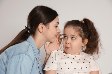 Photo of Teenage girl whispering secret to her cute little sister on white background