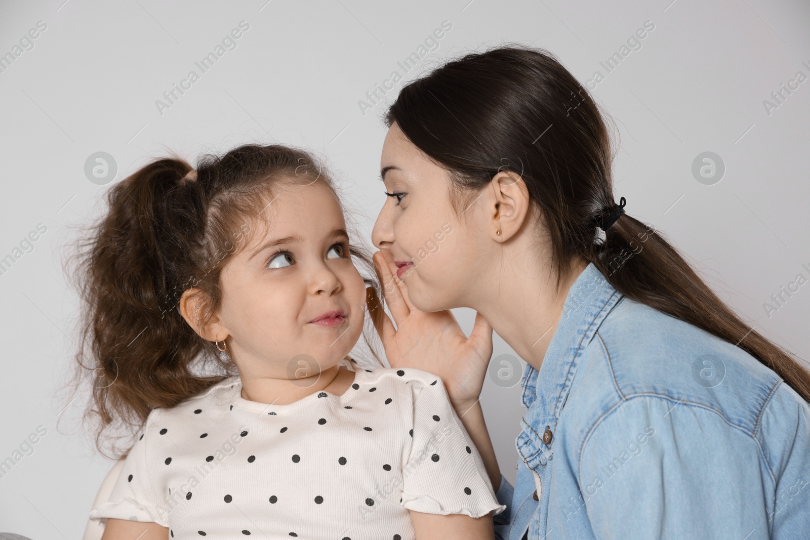 Photo of Teenage girl whispering secret to her cute little sister on white background