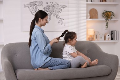 Photo of Teenage girl braiding her sister's hair on sofa at home