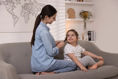 Photo of Teenage girl braiding her sister's hair on sofa at home