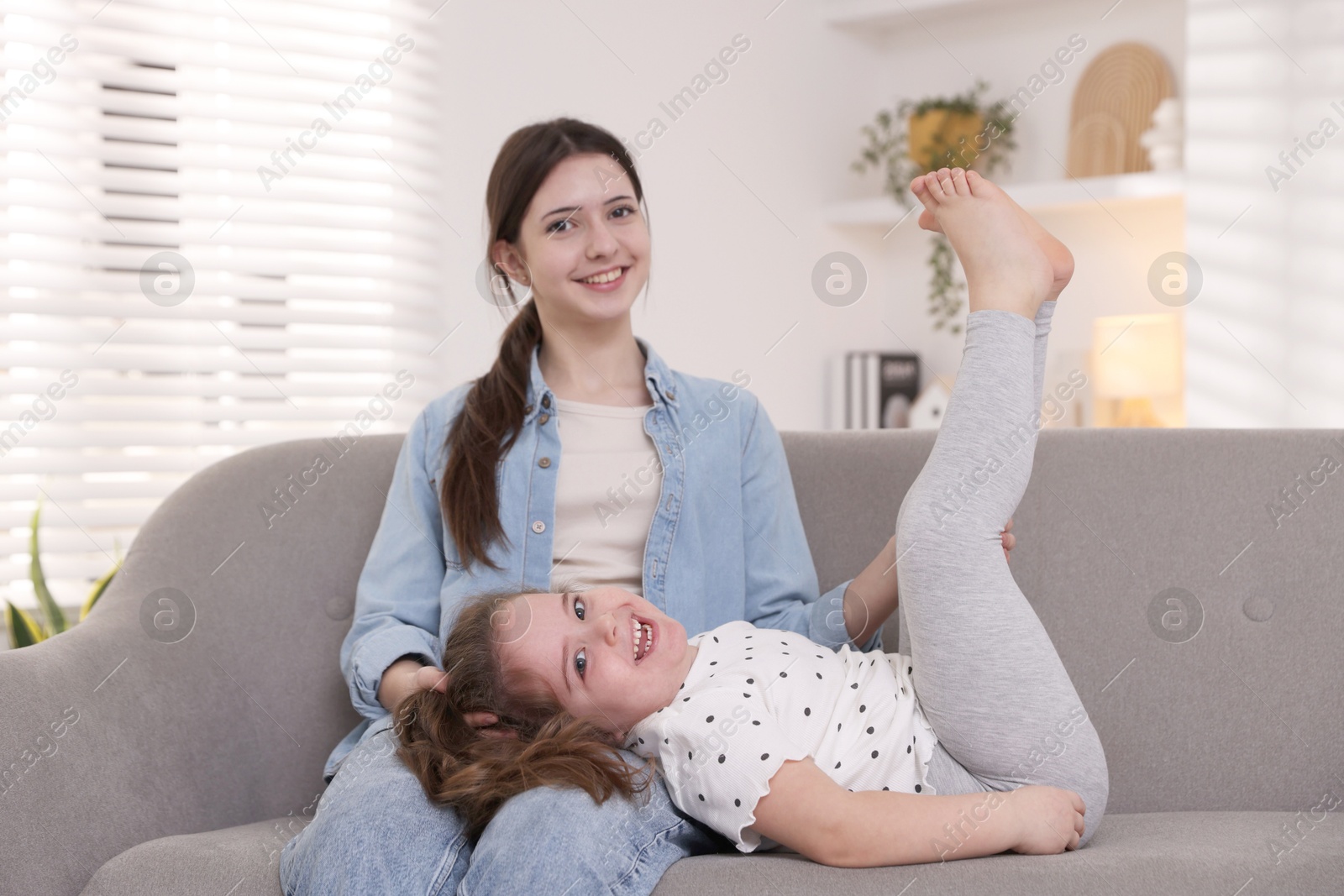 Photo of Cute little girl and her sister on sofa at home