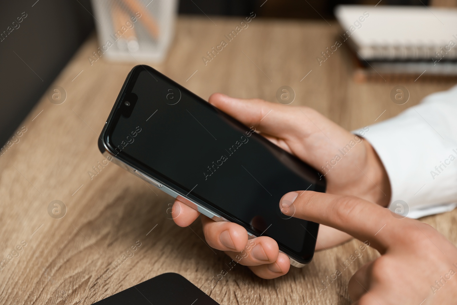 Photo of Man using smartphone with blank screen at wooden table, closeup