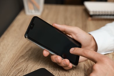 Photo of Man using smartphone with blank screen at wooden table, closeup