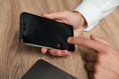 Photo of Man using smartphone with blank screen at wooden table, closeup