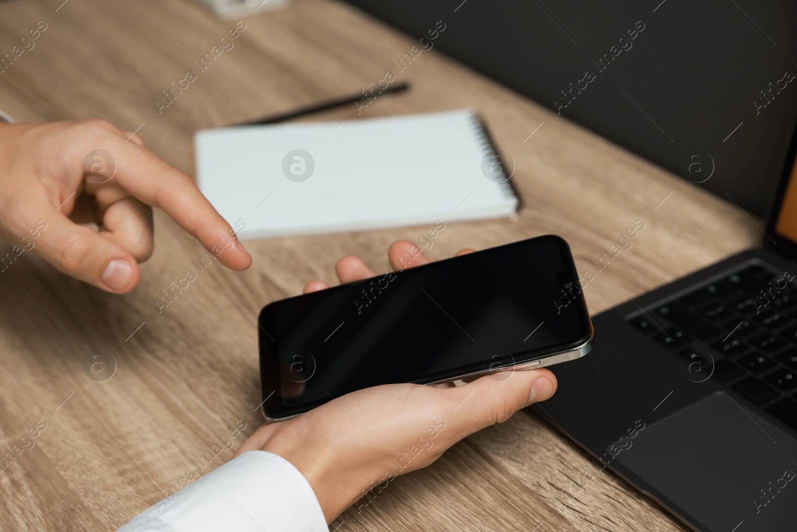 Photo of Man using smartphone with blank screen at wooden table, closeup