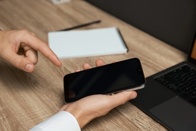 Photo of Man using smartphone with blank screen at wooden table, closeup