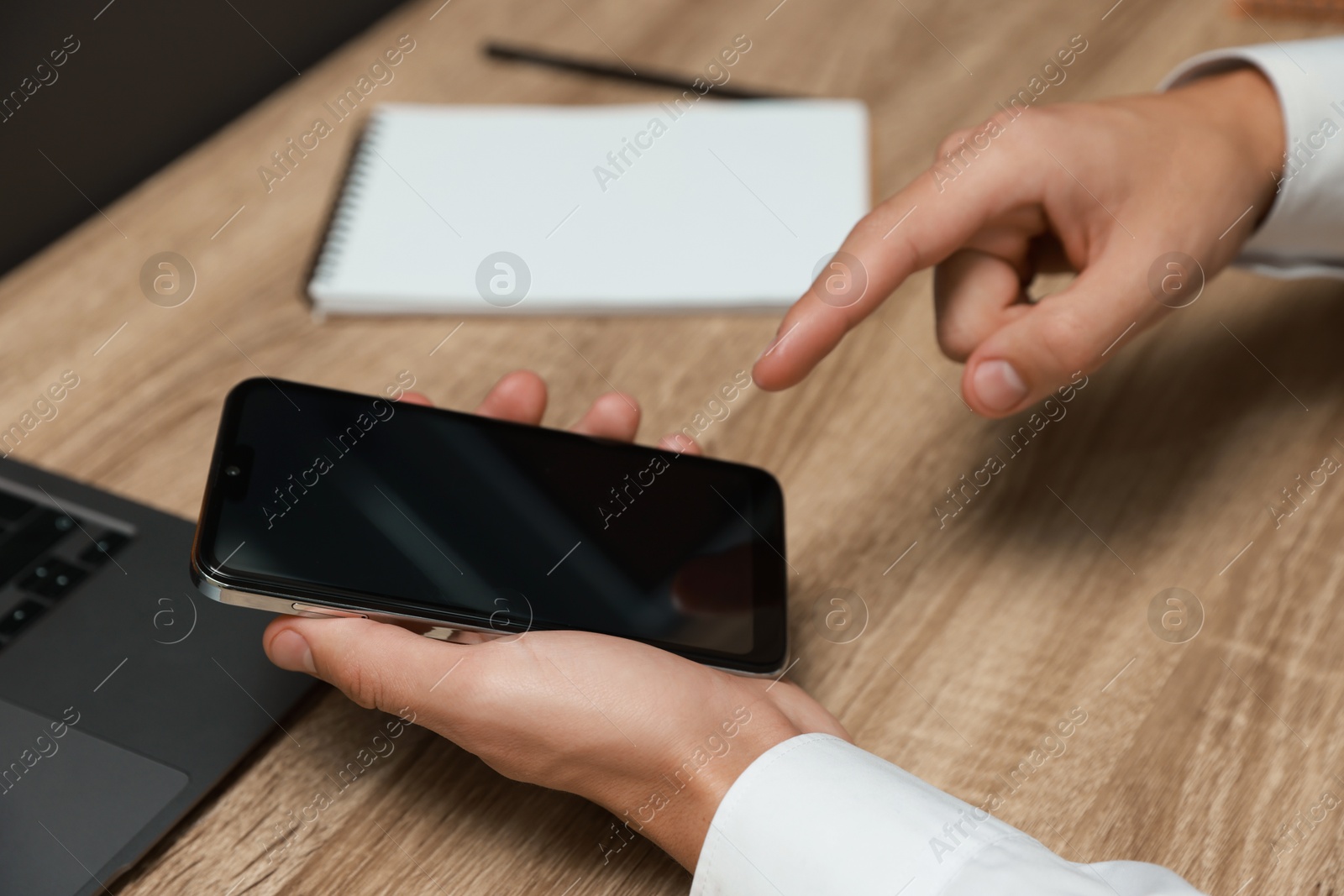 Photo of Man using smartphone with blank screen at wooden table, closeup