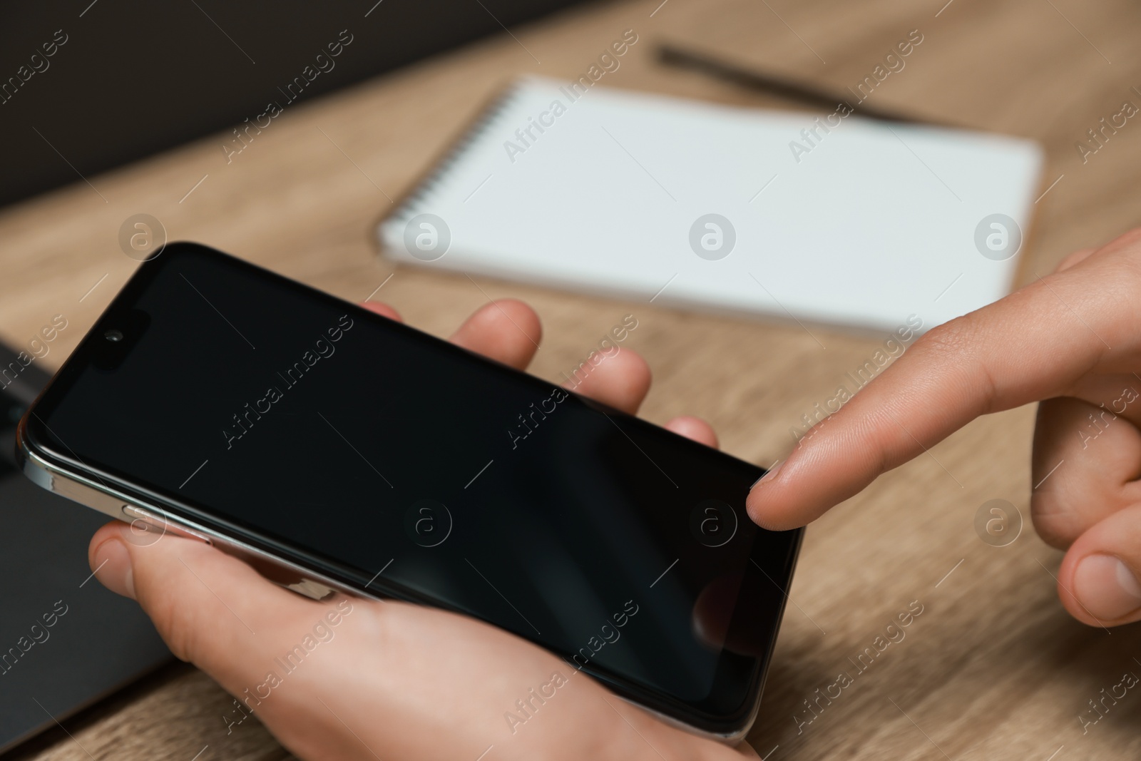 Photo of Man using smartphone with blank screen at wooden table, closeup