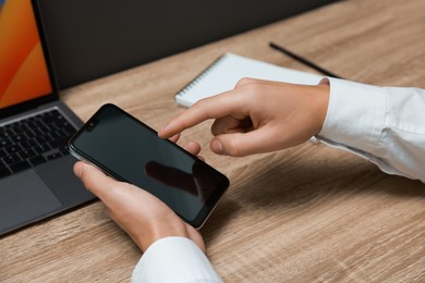 Photo of Man using smartphone with blank screen at wooden table, closeup