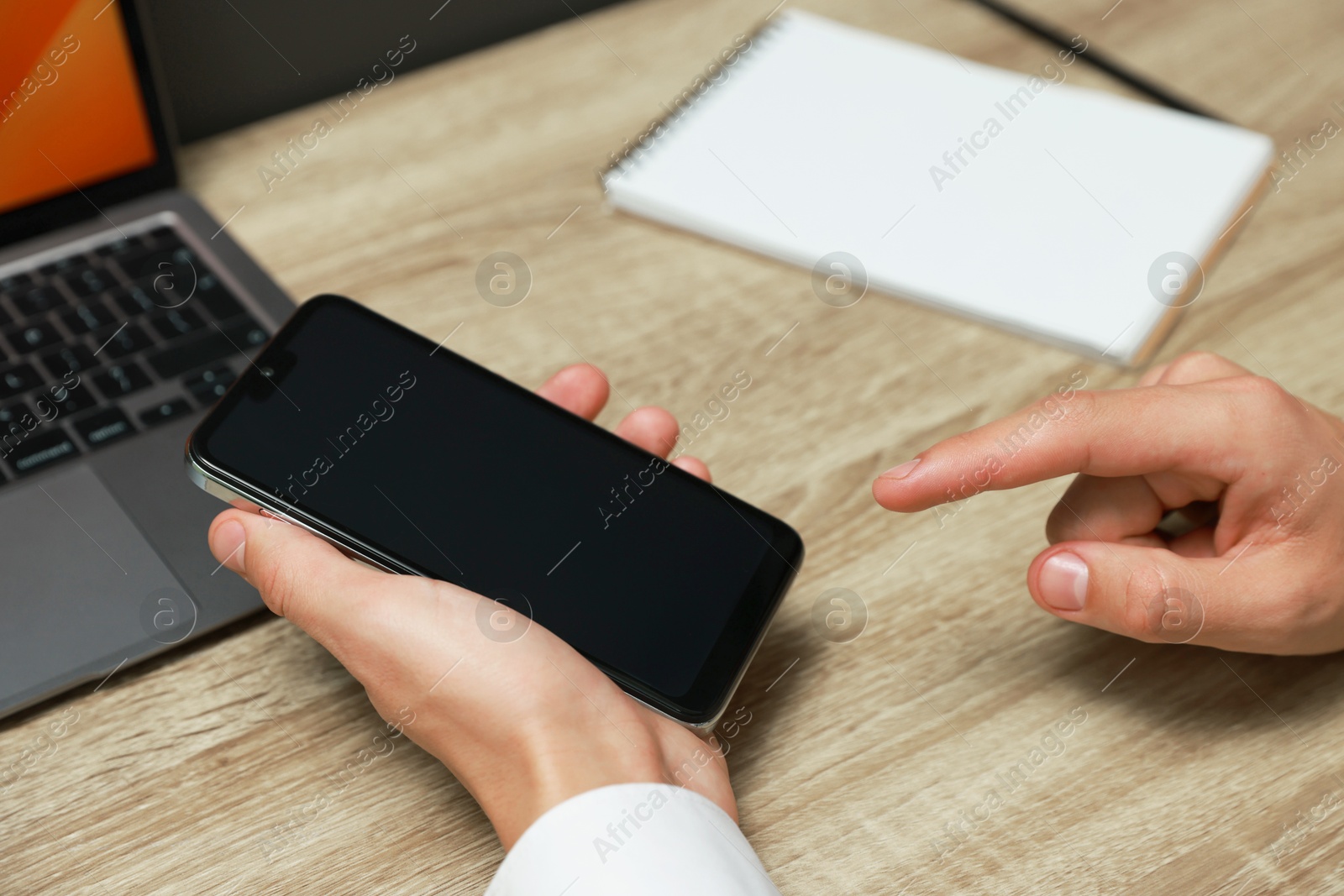 Photo of Man using smartphone with blank screen at wooden table, closeup