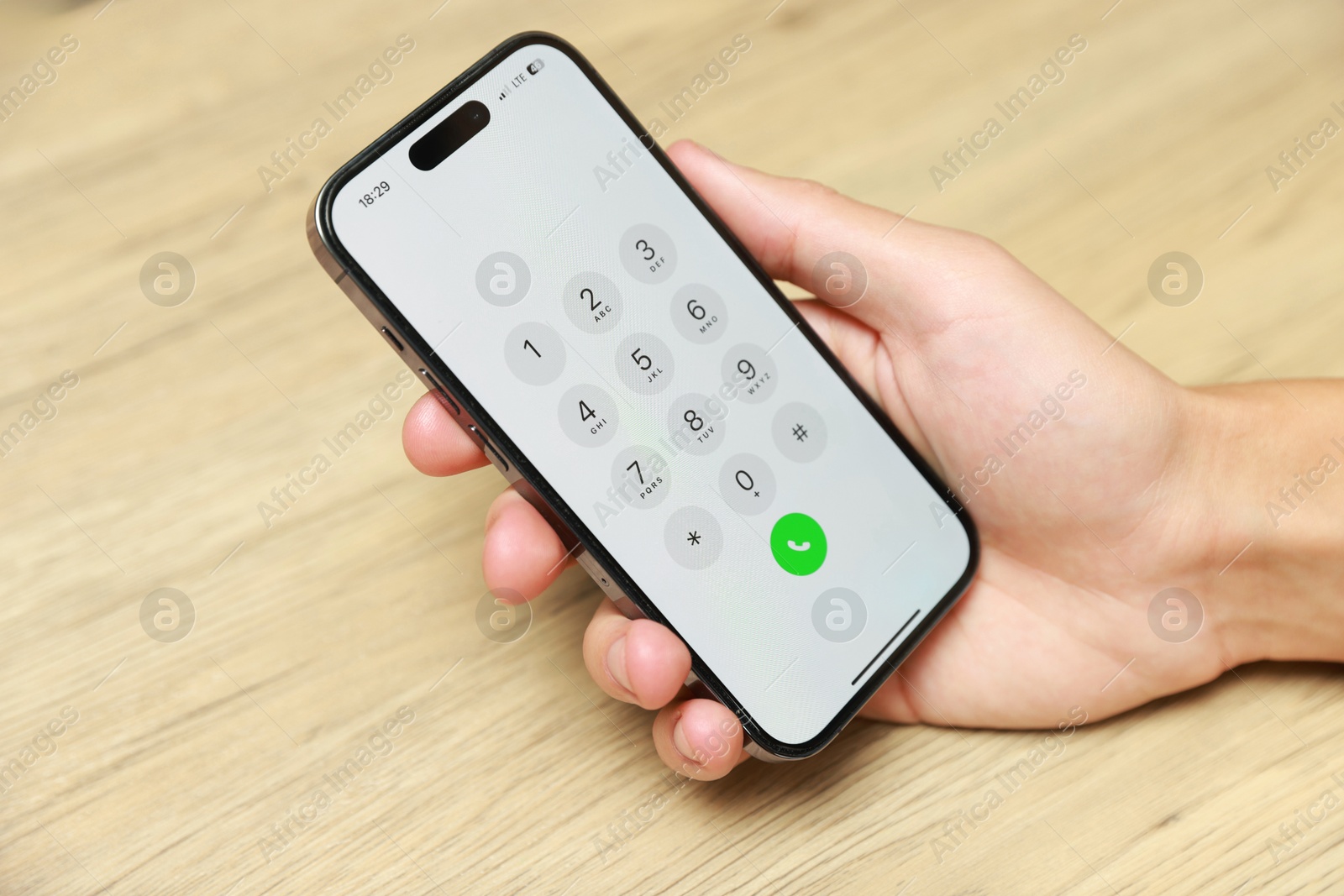 Photo of Man holding smartphone with keypad at wooden table, closeup